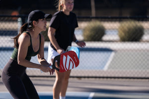 Two women playing pickleball on a court, one holding a paddle.