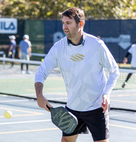 A man preparing to serve in pickleball, holding a paddle with a yellow ball in play.