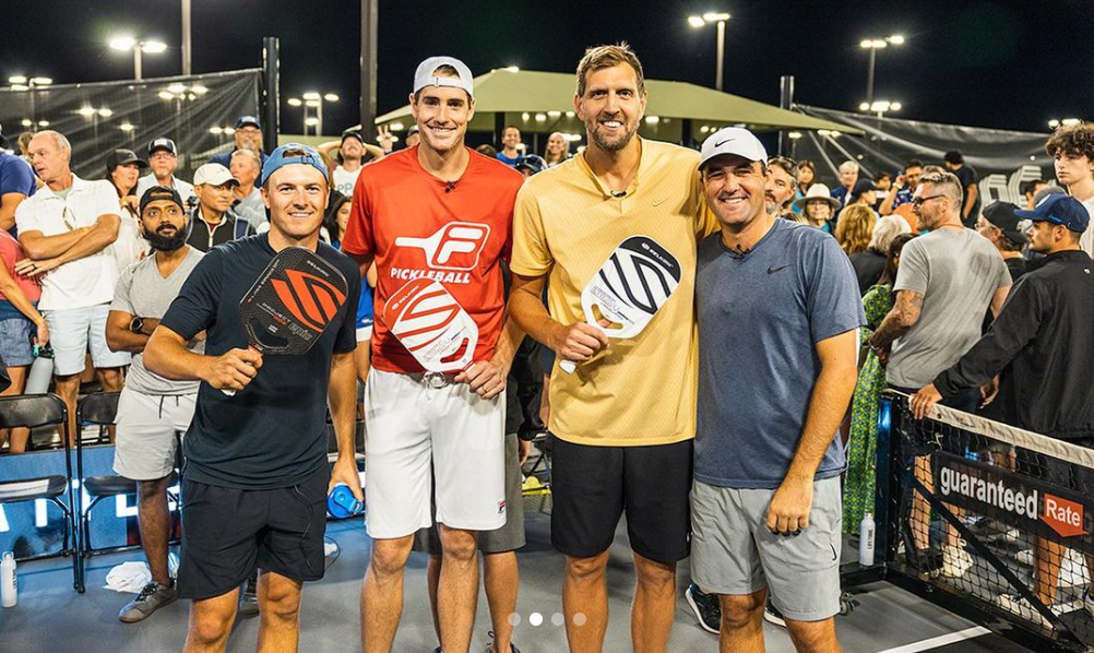 Four pickleball players posing with paddles at a crowded event.