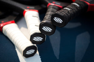 Four pickleball paddles with different grip sizes on a court surface.