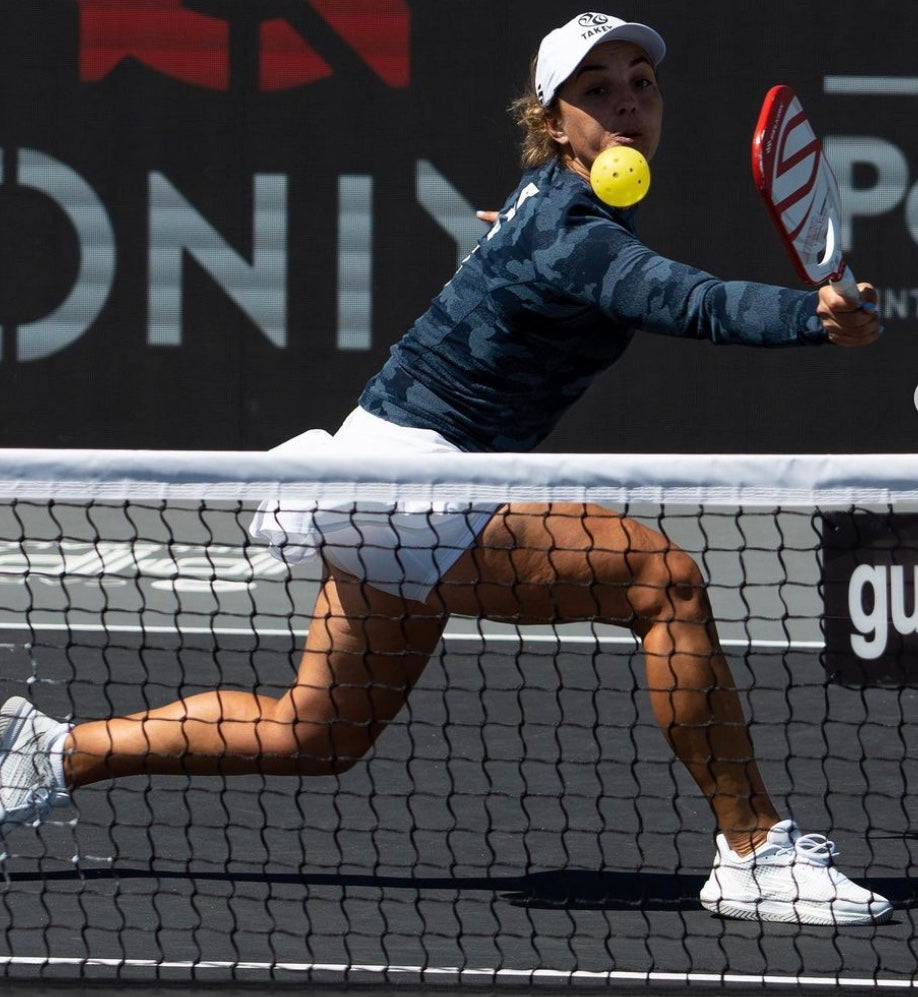 A player in a blue camo top hitting a pickleball during a match.