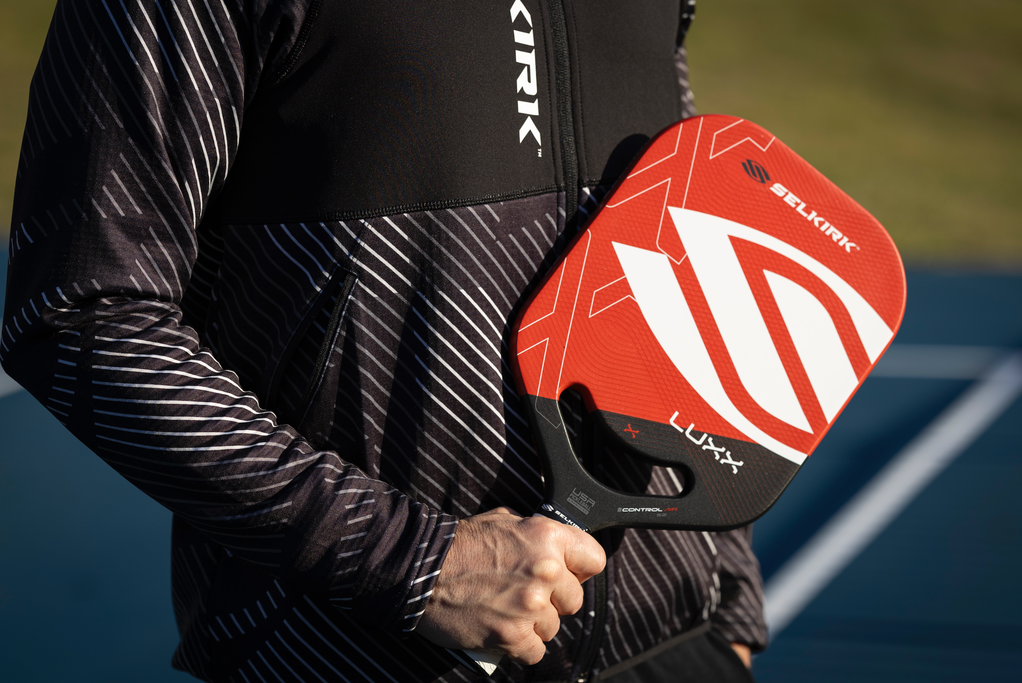 A player holding a red and black pickleball paddle, showcasing its design.