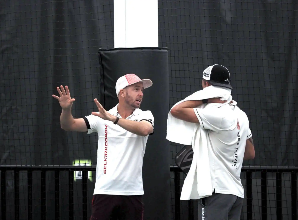 A pickleball coach gestures while talking to a player during practice.