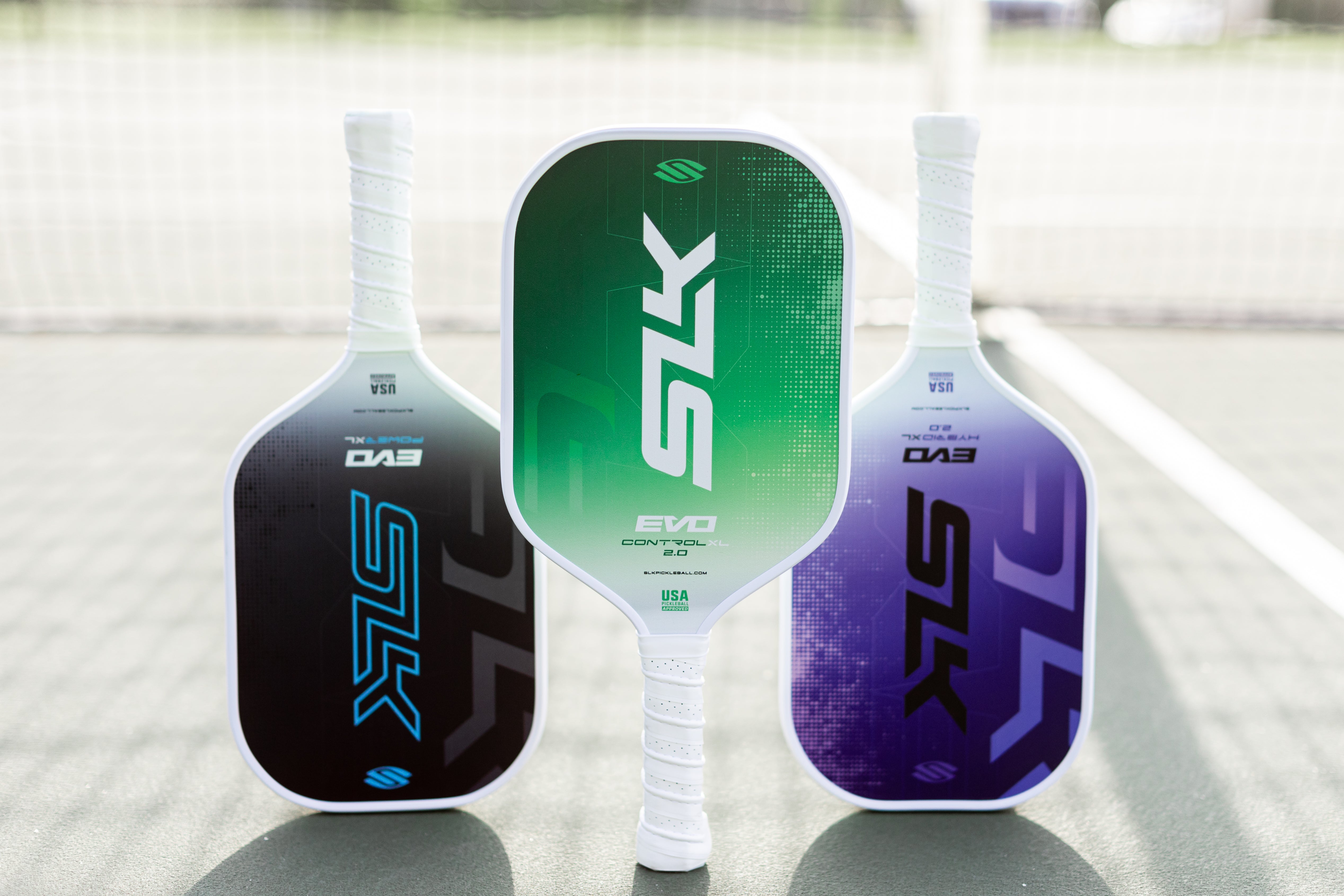 Three pickleball paddles in green, white, and purple on a court.