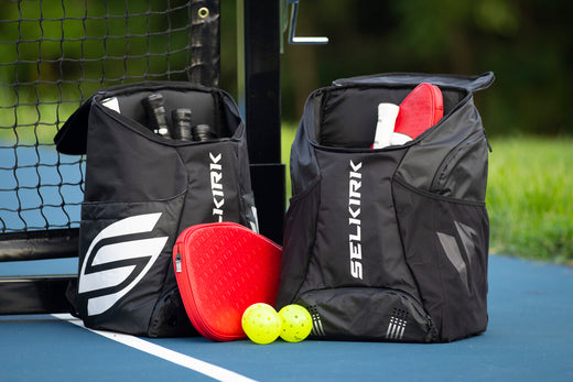 Two open Selkirk pickleball backpacks on a court, showing storage for paddles and balls.