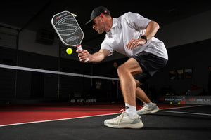 A player wearing pickleball shoes, preparing to hit a ball with a paddle on a court.