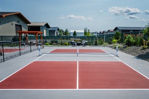 A view of a pickleball court with red surfaces and surrounding buildings.