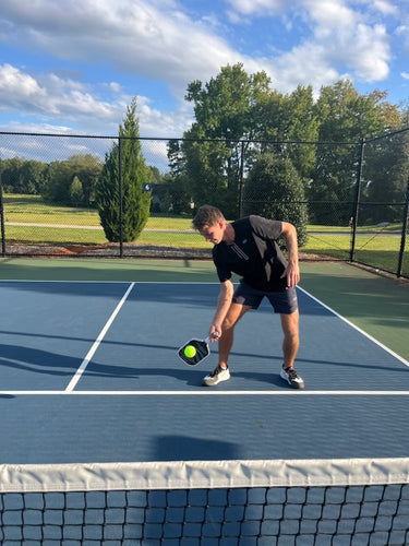 A player demonstrating a pickleball serve with a VANGUARD Pro paddle on a court