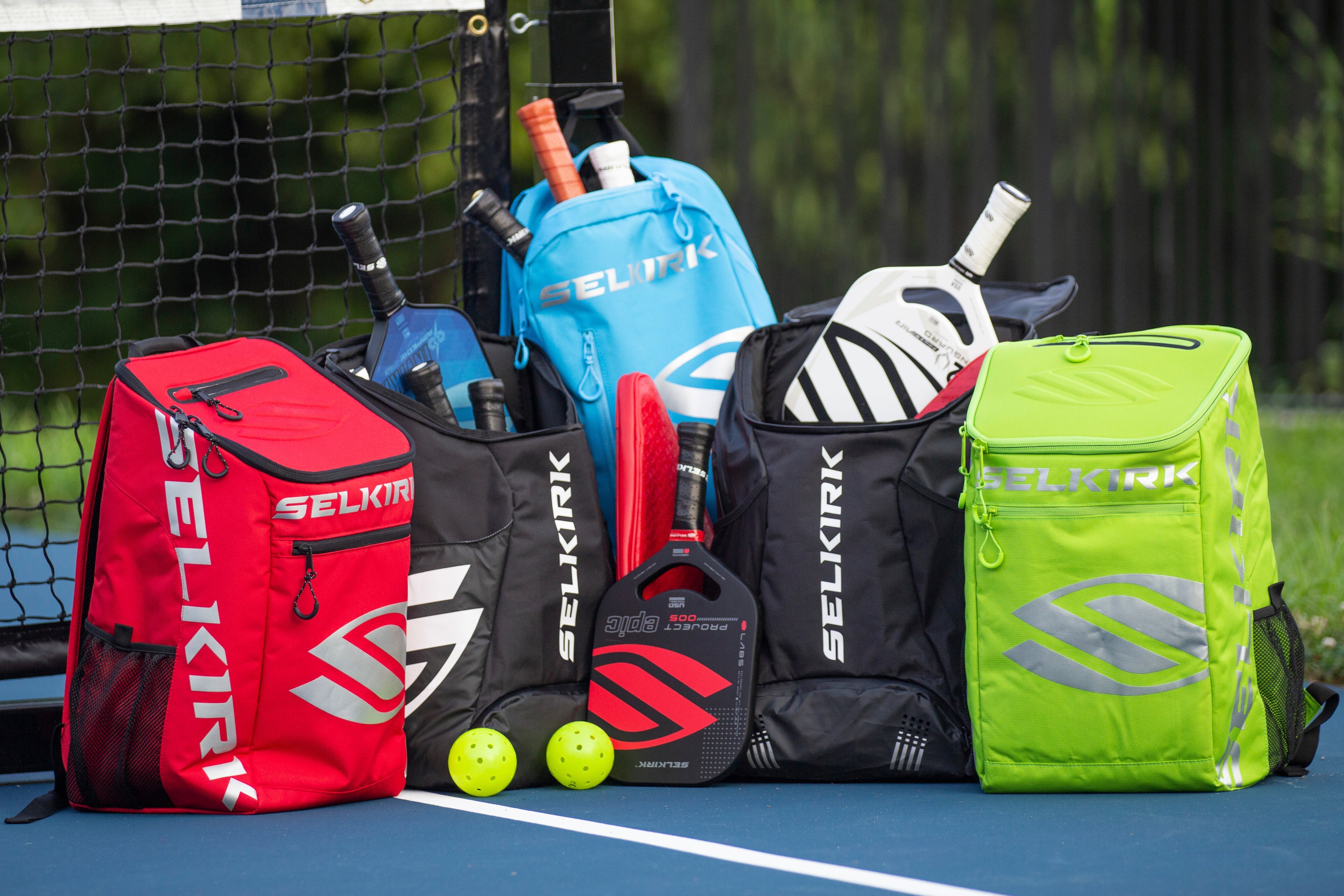 Colorful Selkirk bags filled with paddles and balls on a pickleball court.