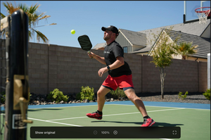 A player preparing to hit a pickleball on a court with a net and hoop in the background.