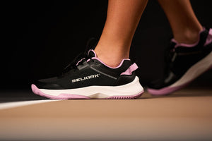 Close-up of Selkirk pickleball shoes in black and pink on a court surface.