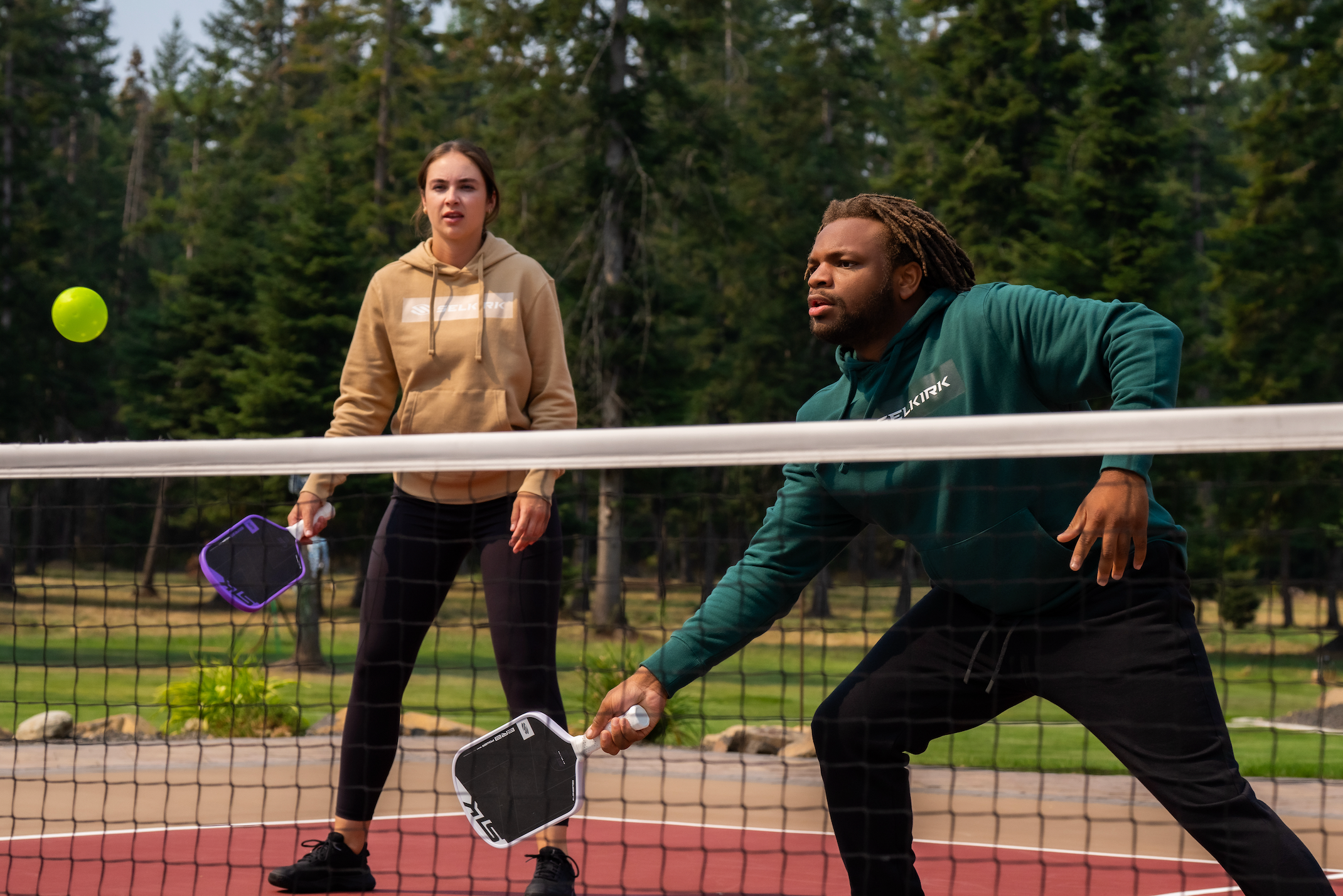 A woman watches as a man prepares to hit a forehand volley.