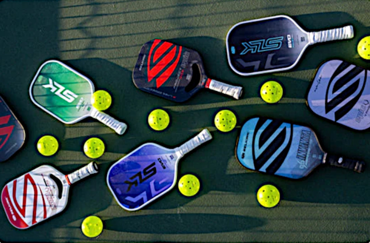 A collection of pickleball paddles and balls on a court surface.