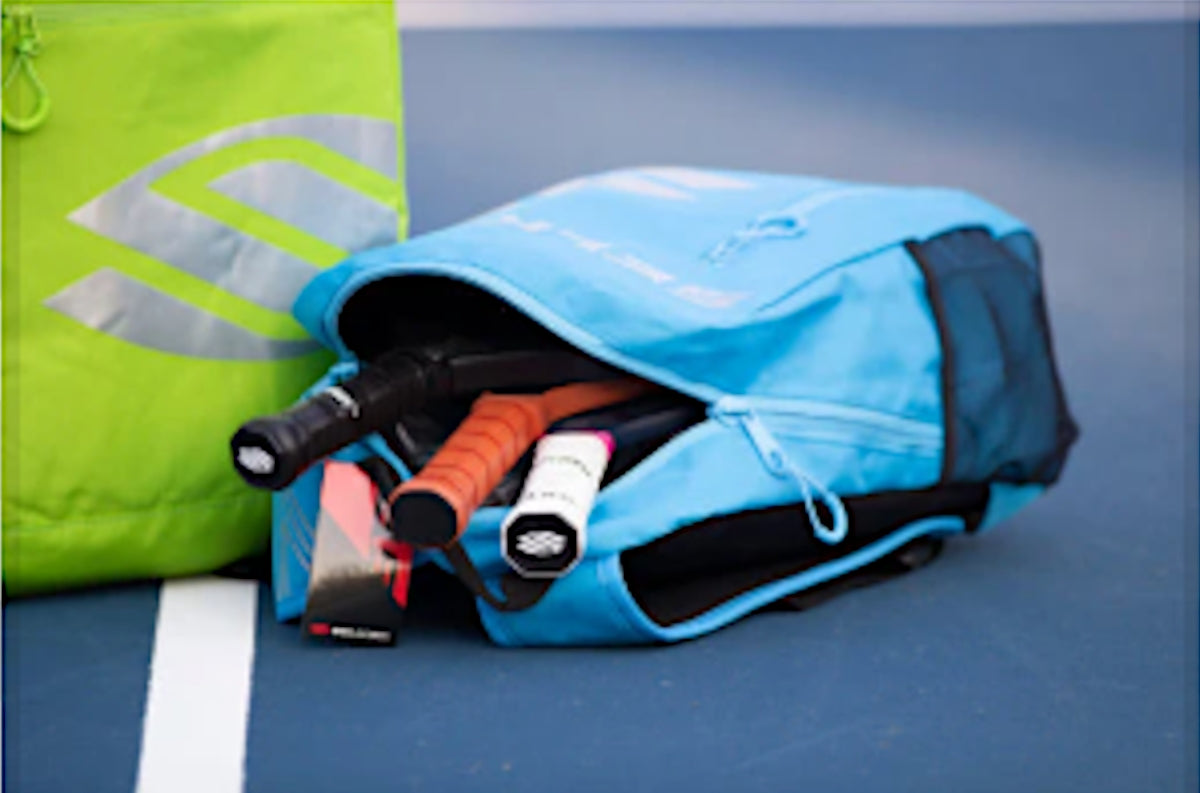 Blue Selkirk pickleball bag with many pickleball accessories on a pickleball court.