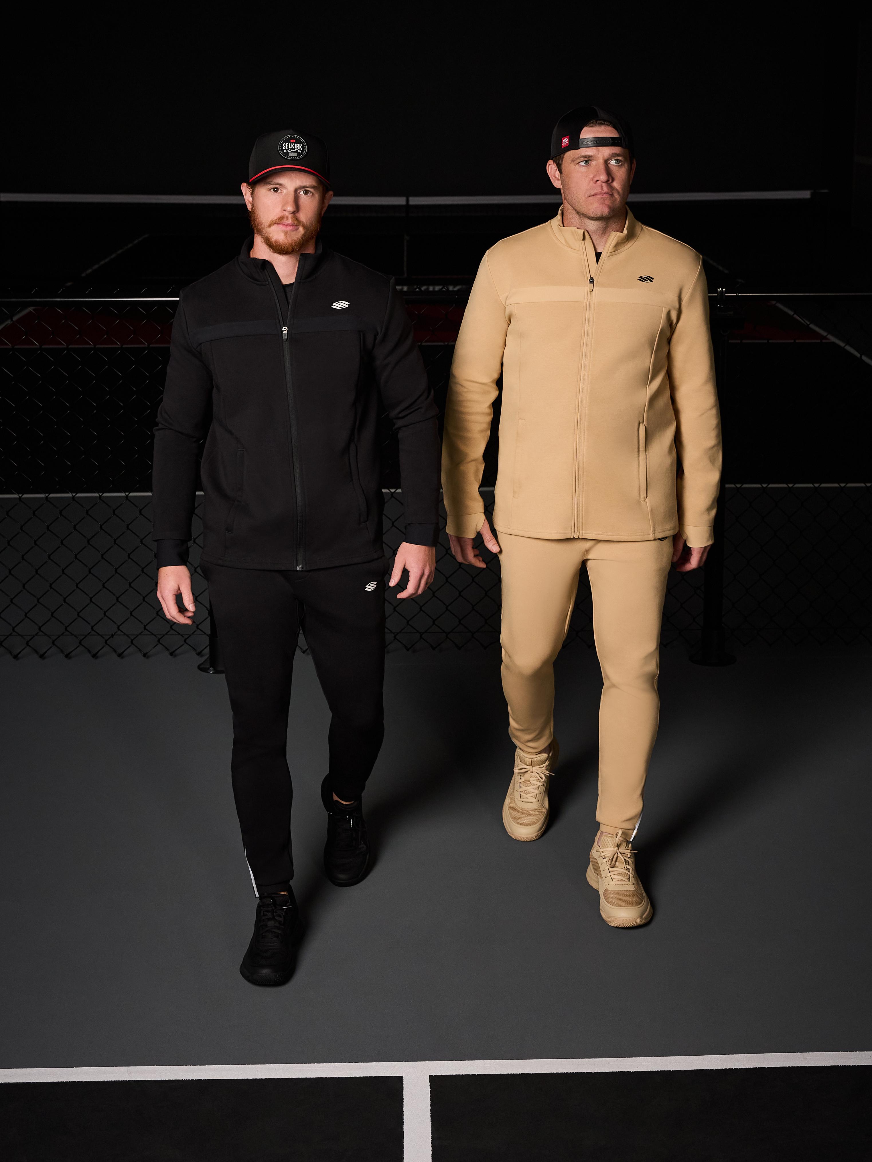 Two men wearing athletic joggers and jackets, one in black and one in beige, on a court.