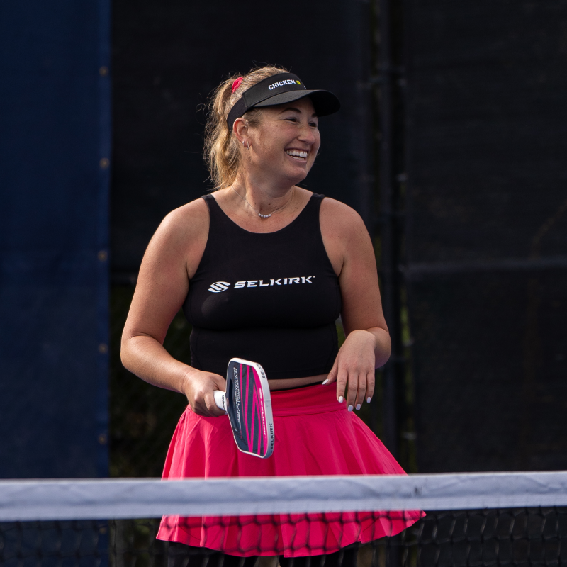 Female pickleball player wearing a Selkirk tanktop and pink skirt, holding a pickleball paddle and smiling