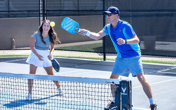 A man and a woman smile as they pickleball up near the net. 