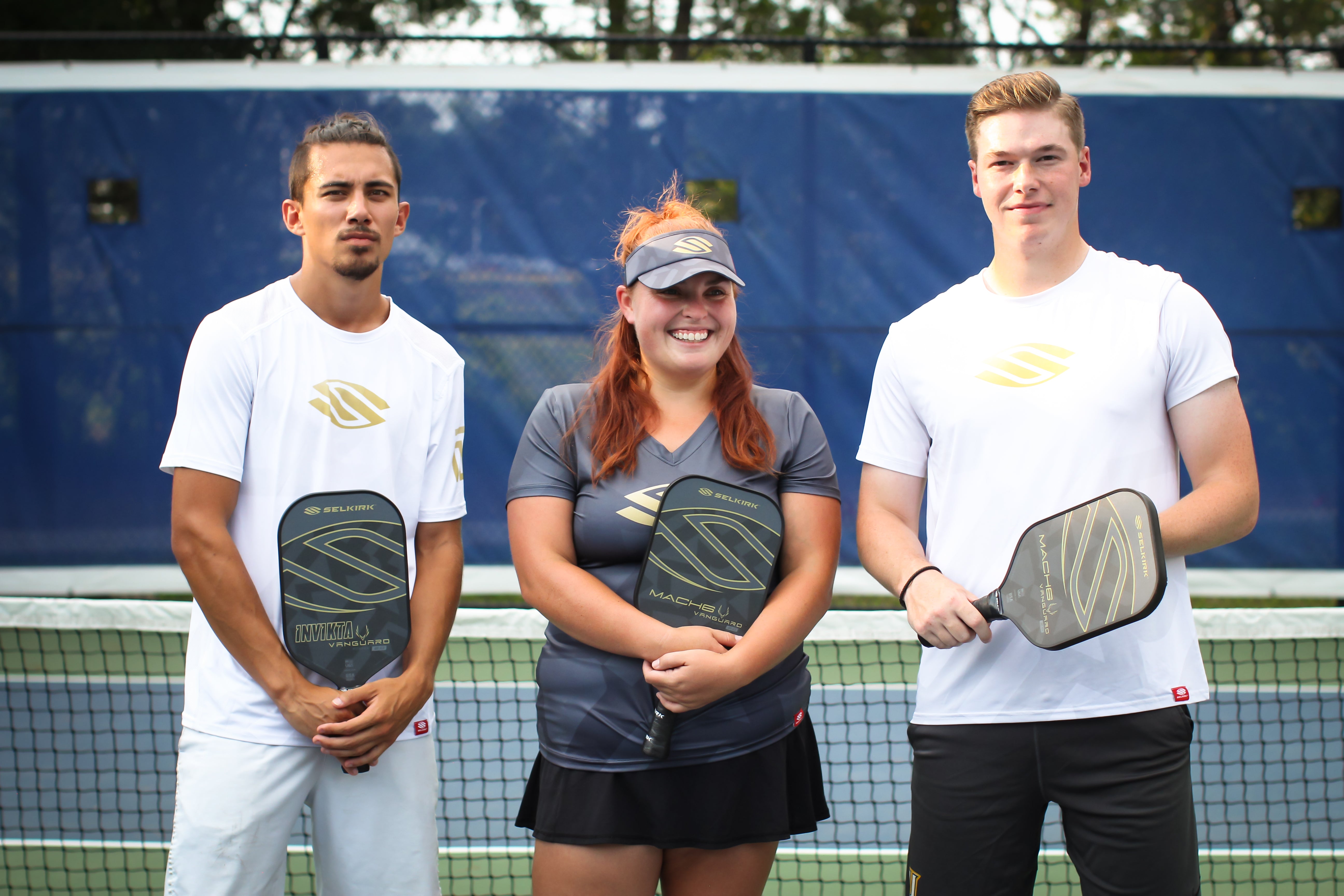 Three pickleball players posing with paddles on a court