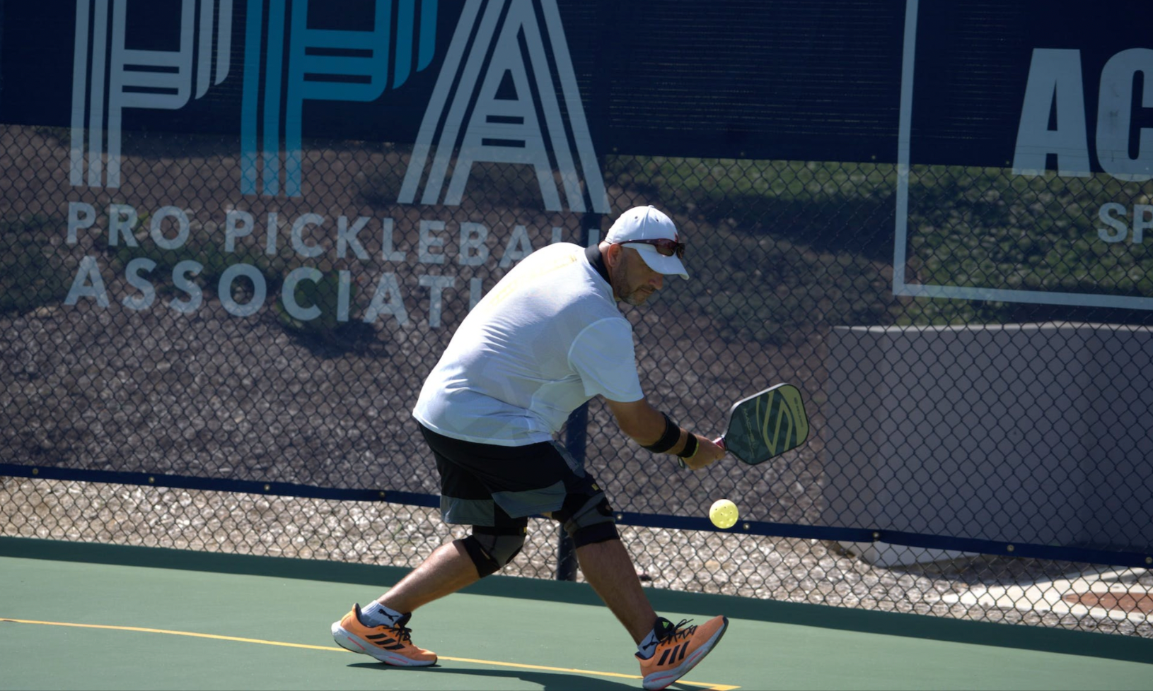 A man playing pickleball on a court, wearing knee braces and preparing to hit a ball.
