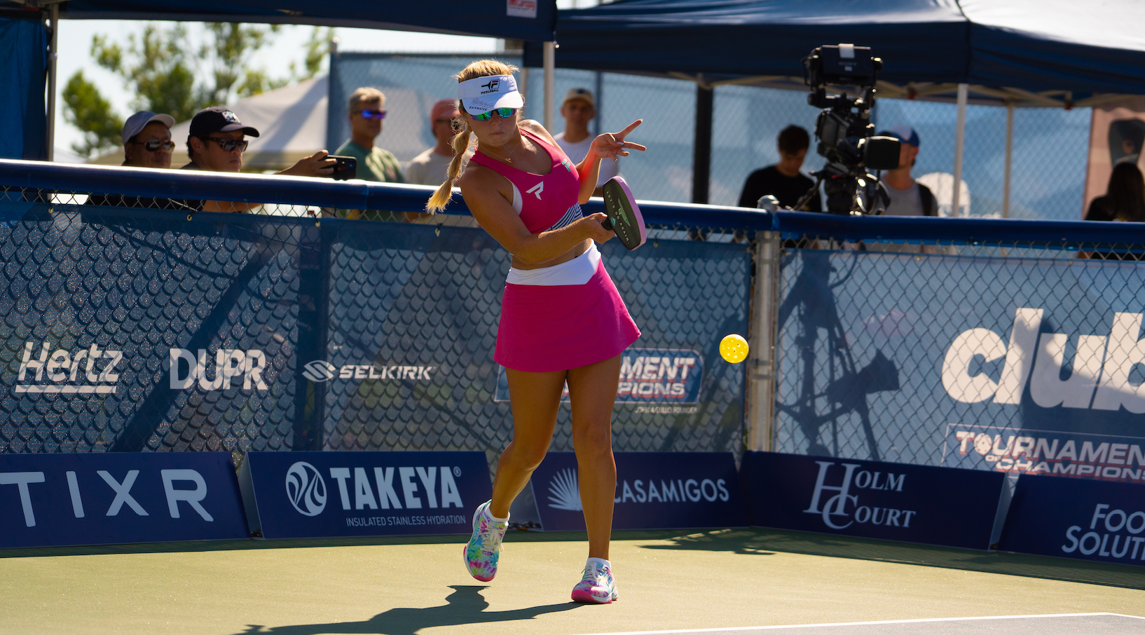 A female player in a pink outfit serves during the PPA Tournament of Champions.
