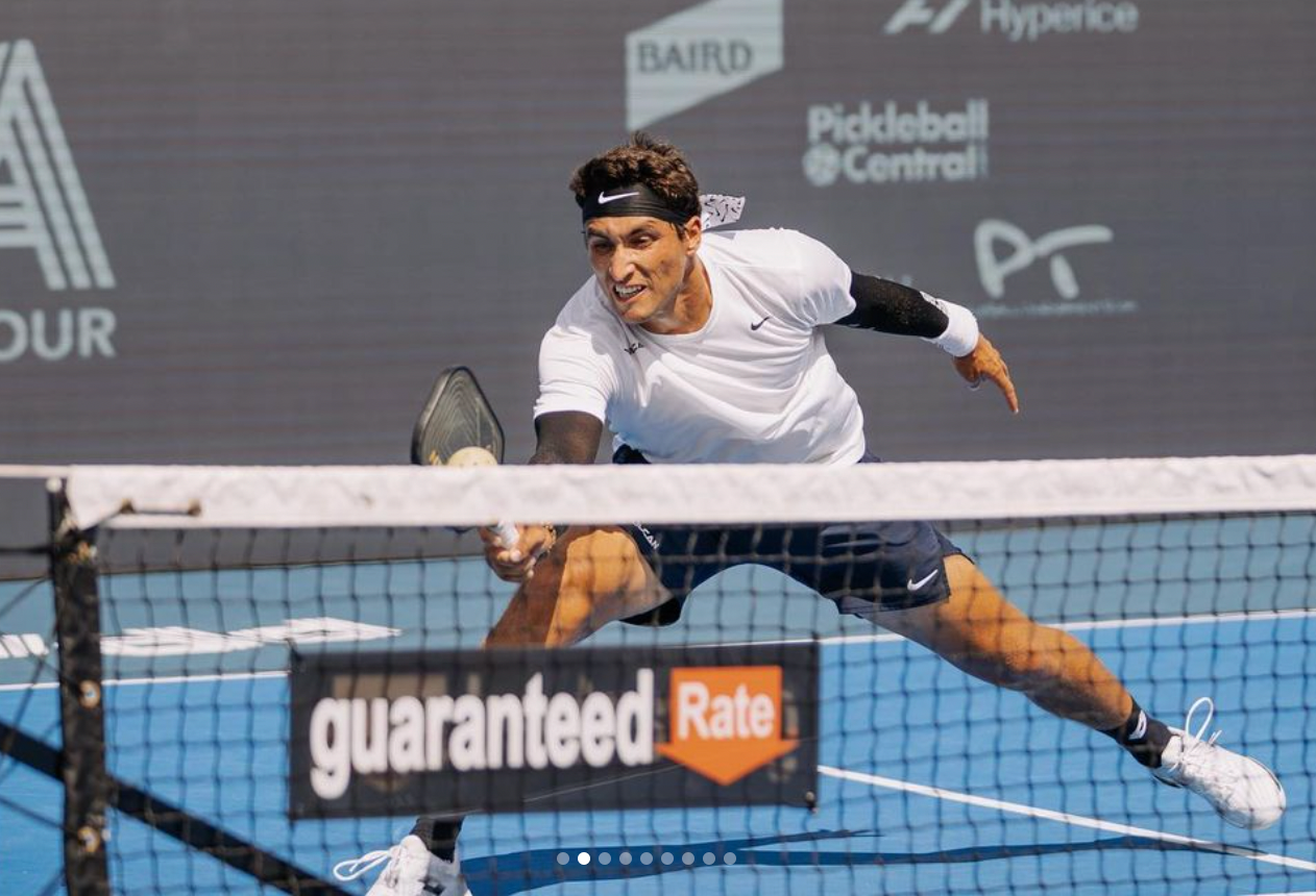 A player diving to hit a pickleball near the net with a 'guaranteed Rate' sign in the foreground.