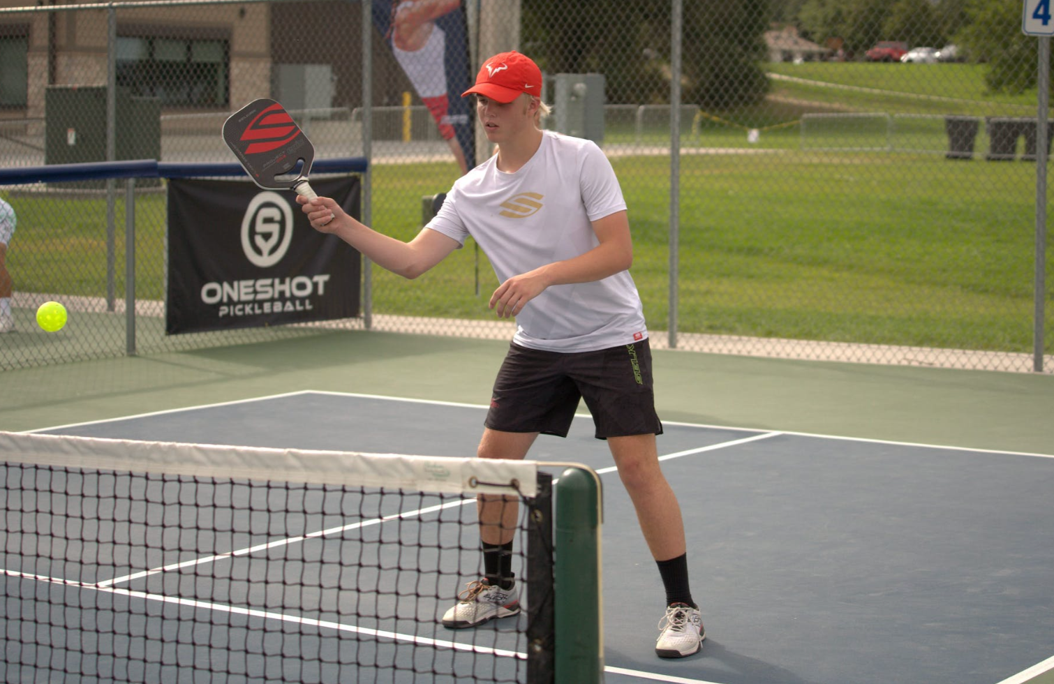 A young player preparing to hit a pickleball on the court.