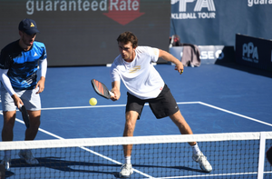 Two players practicing pickleball on a court, one hitting a ball with a paddle.
