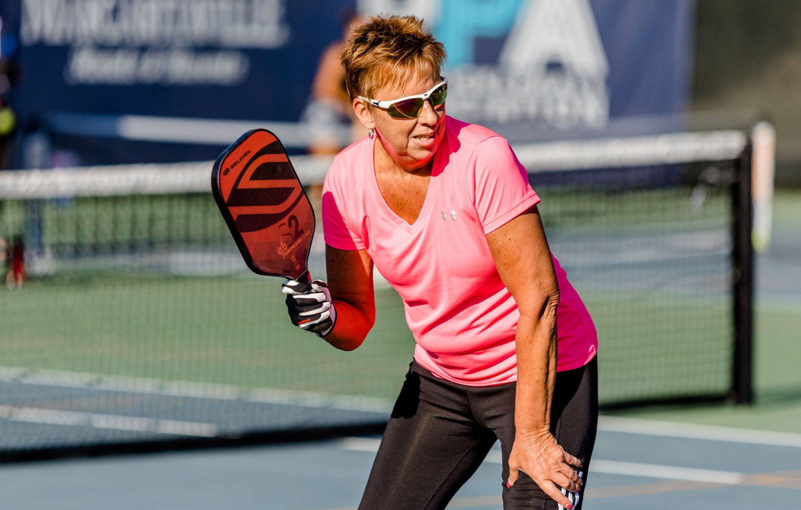 A woman in a pink shirt playing pickleball, preparing to hit the ball.