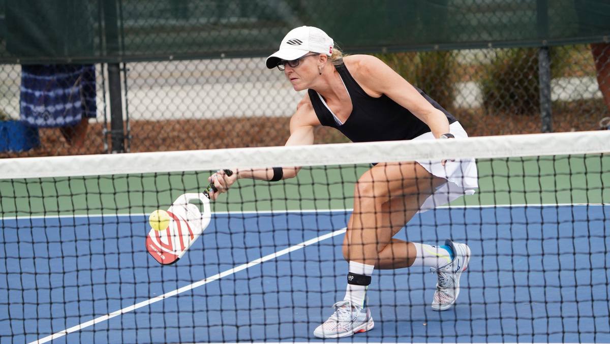 Susannah Barr lunges to hit a pickleball near the net on an outdoor court
