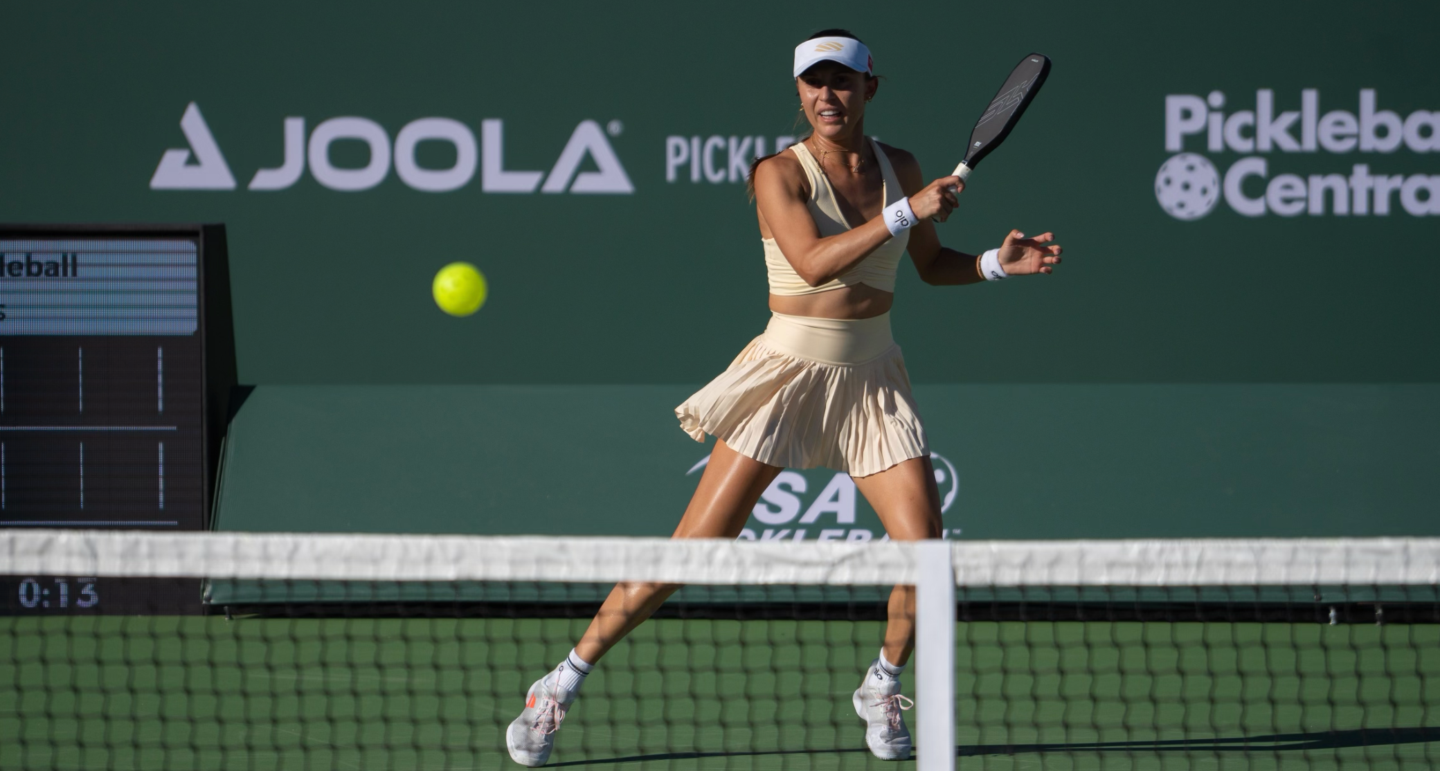A female pickleball player in a beige outfit hitting a ball during a match.