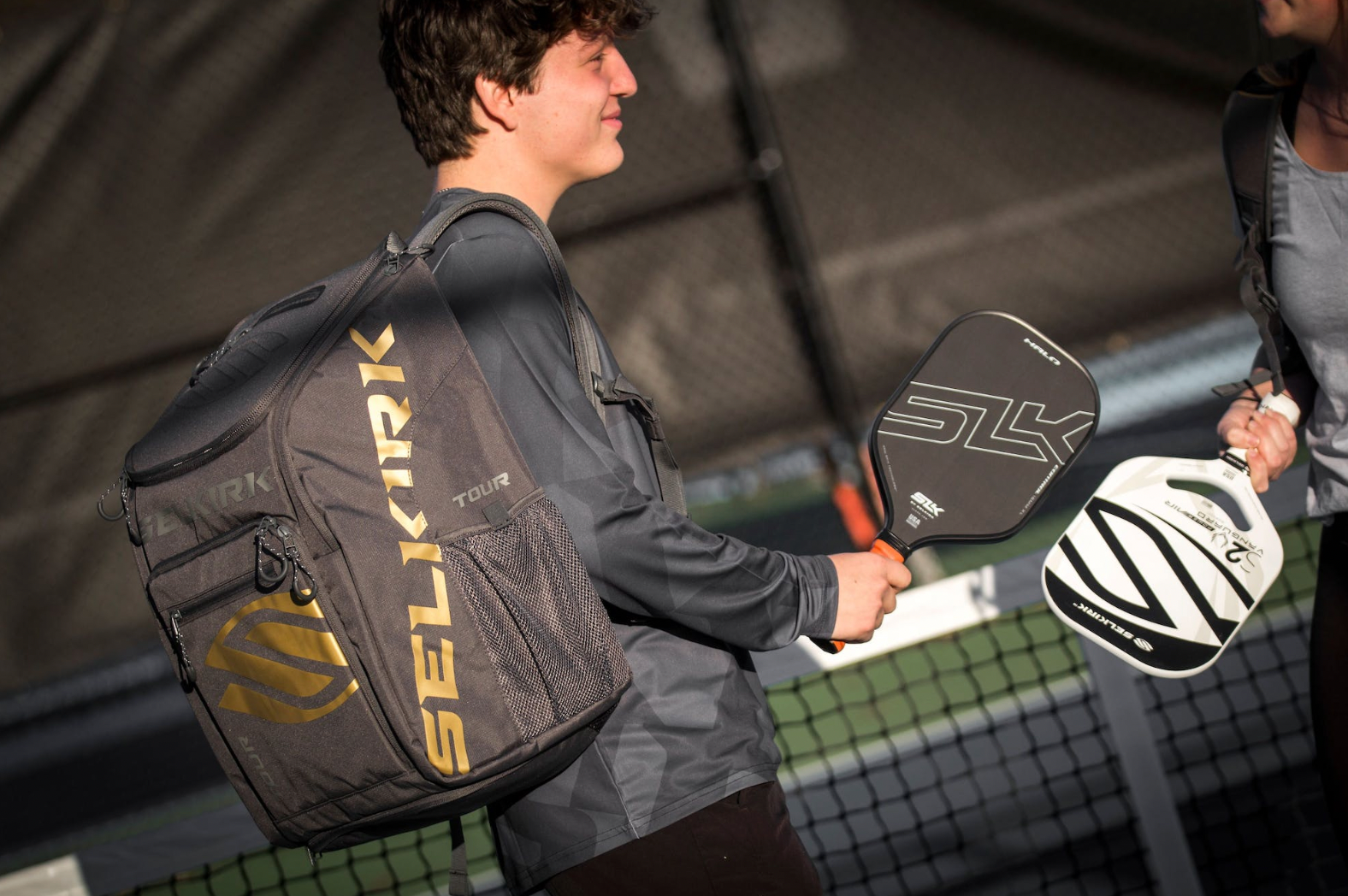 A player holding Selkirk paddles and a backpack on a pickleball court.