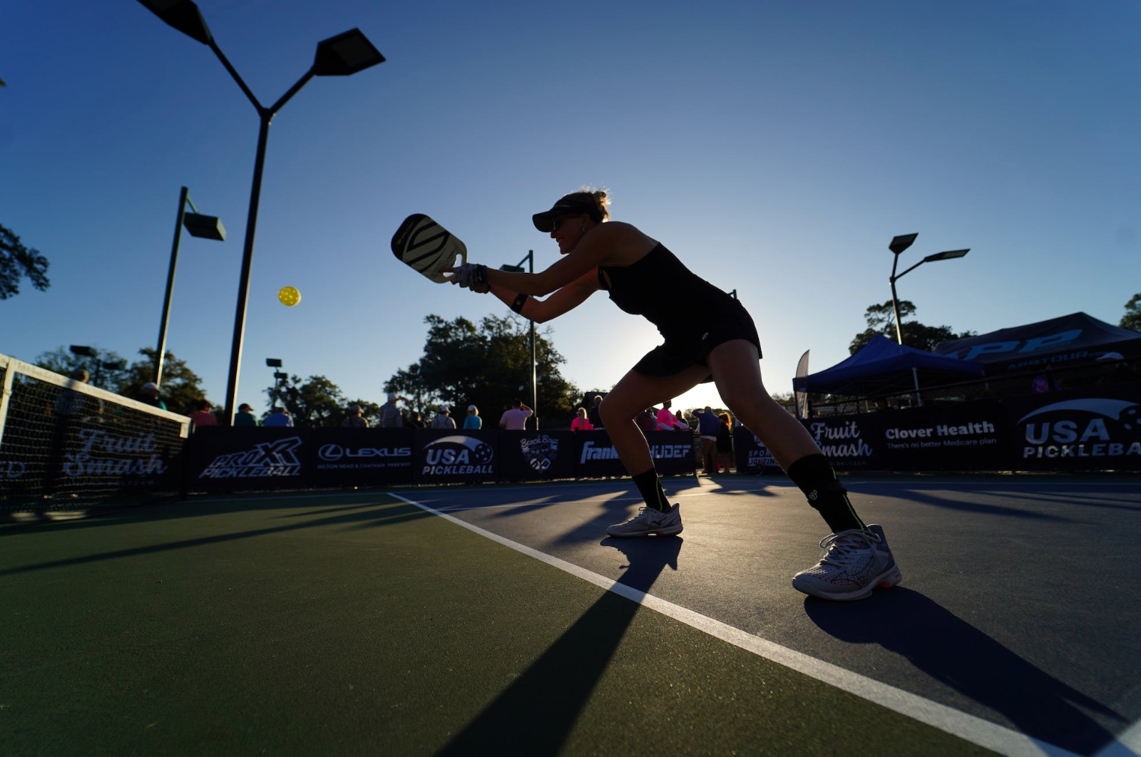 Woman hitting a pickleball with a paddle on an outdoor court during a sunny tournament