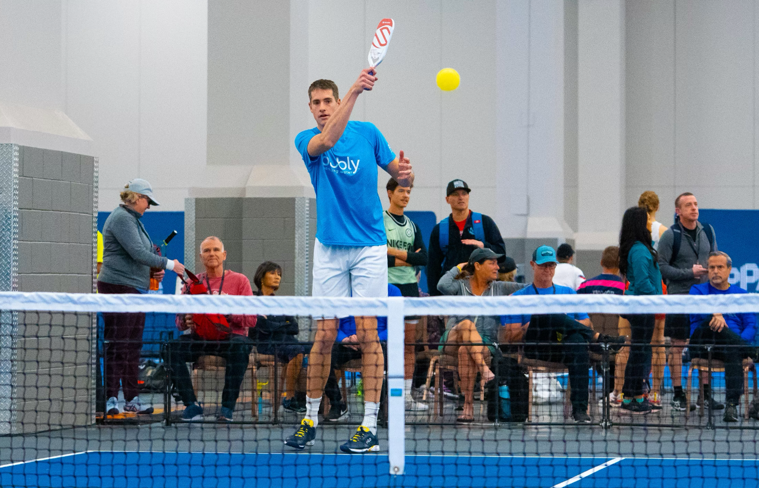A player in a blue shirt prepares to hit a pickleball during a match.
