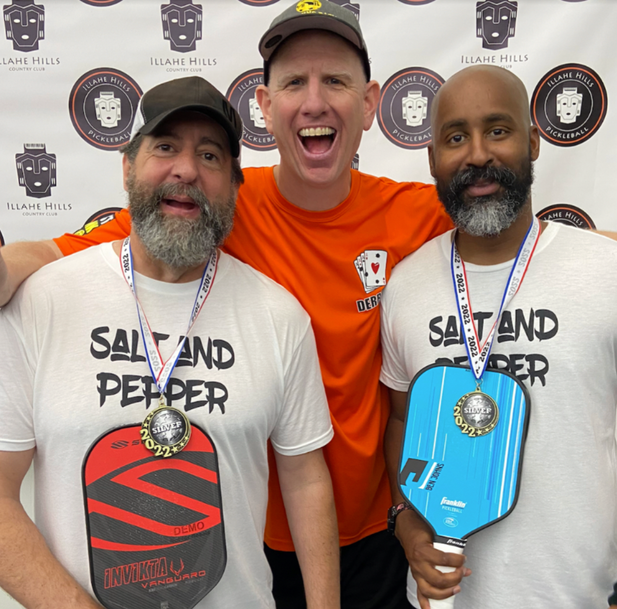 Three men celebrating a pickleball event, two wearing 'Salt and Pepper' shirts and holding paddles.