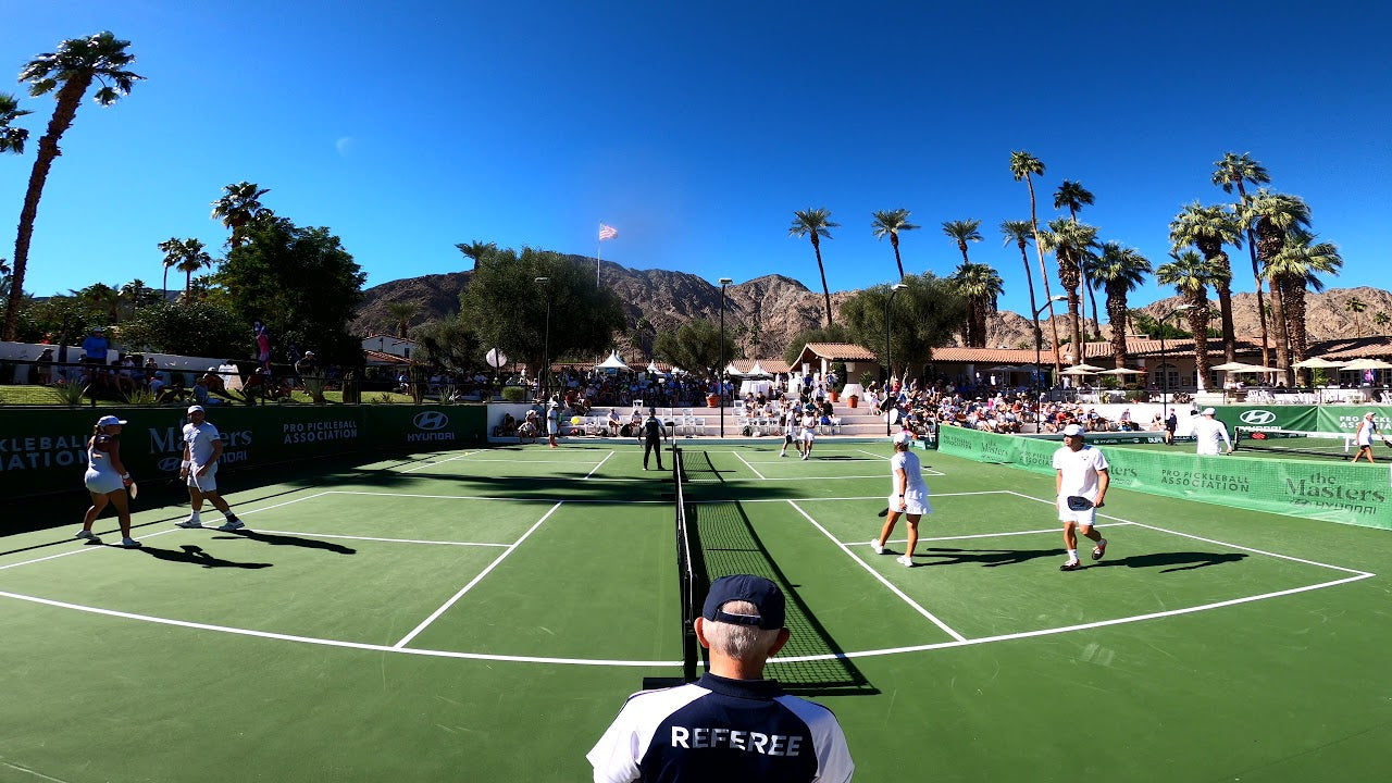 View of a pickleball tournament with players on the court and a referee in the foreground.