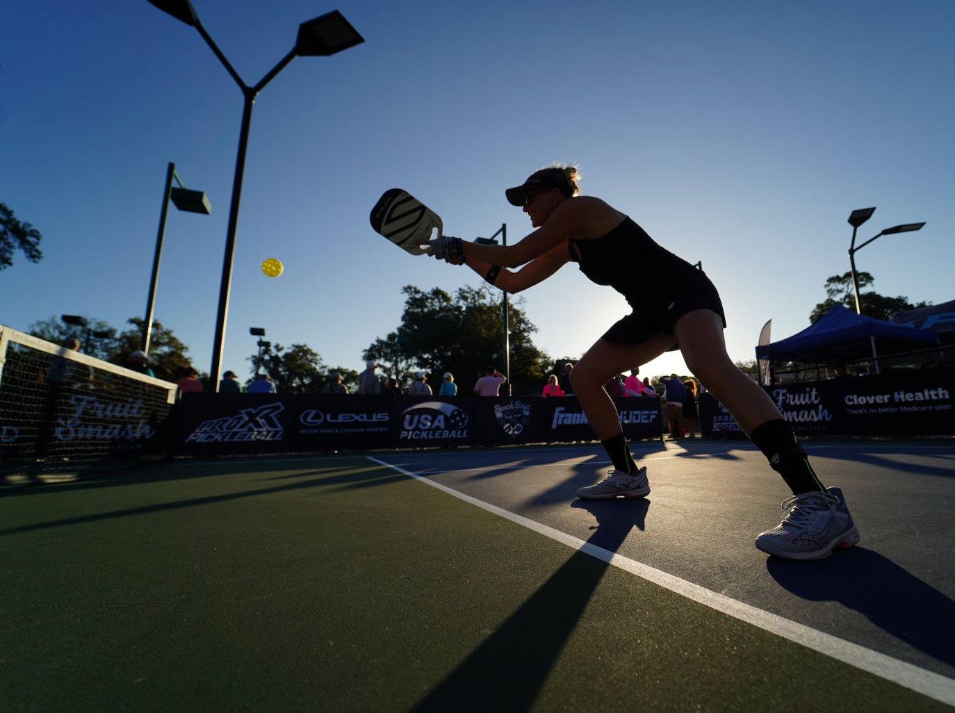 A player preparing to hit a pickleball during a match at sunset.