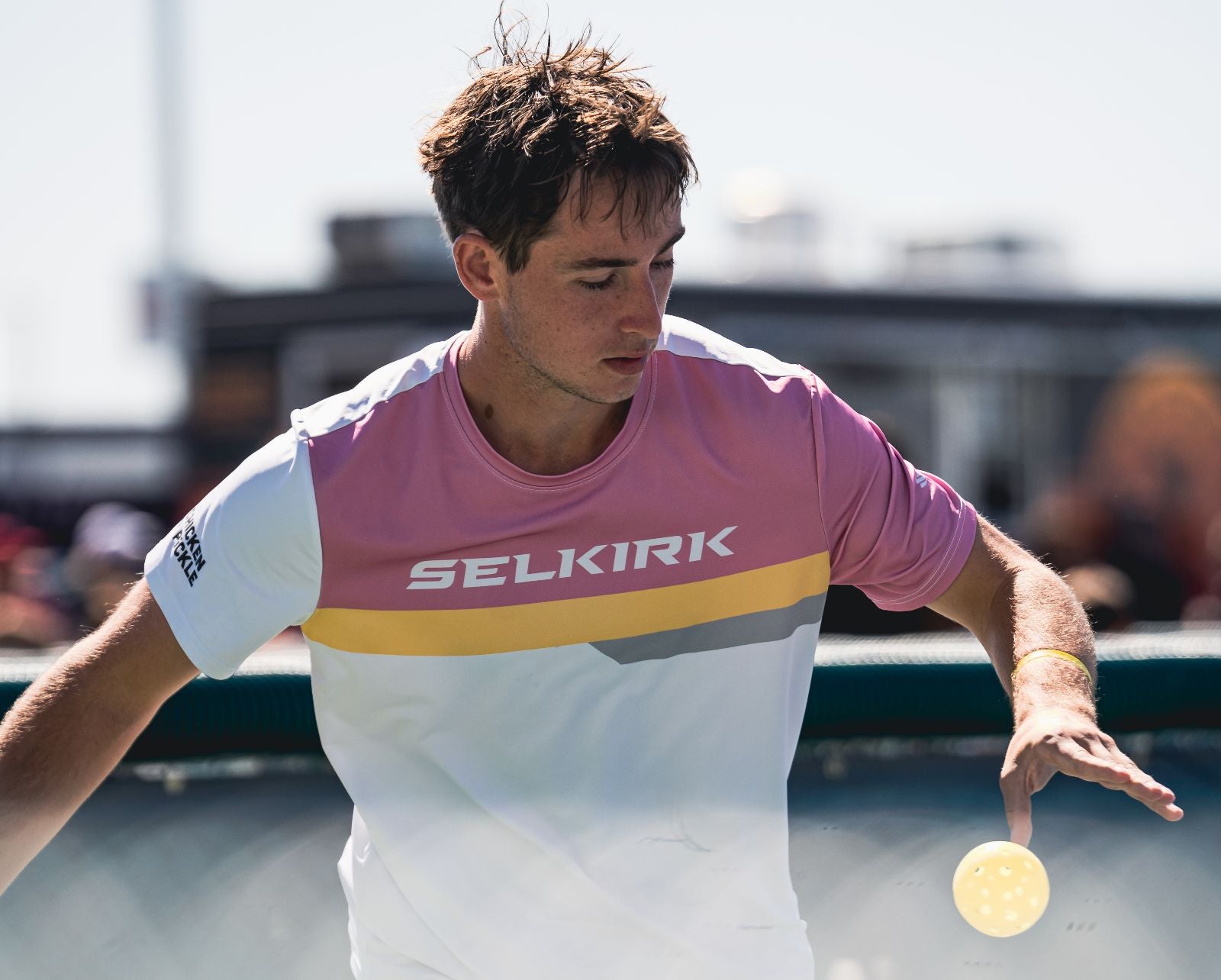 A male pickleball player preparing to serve with a yellow ball.