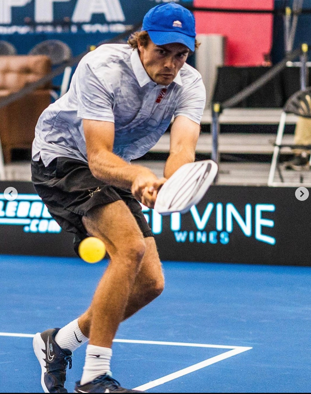 A player in a blue cap hitting a pickleball on a court.