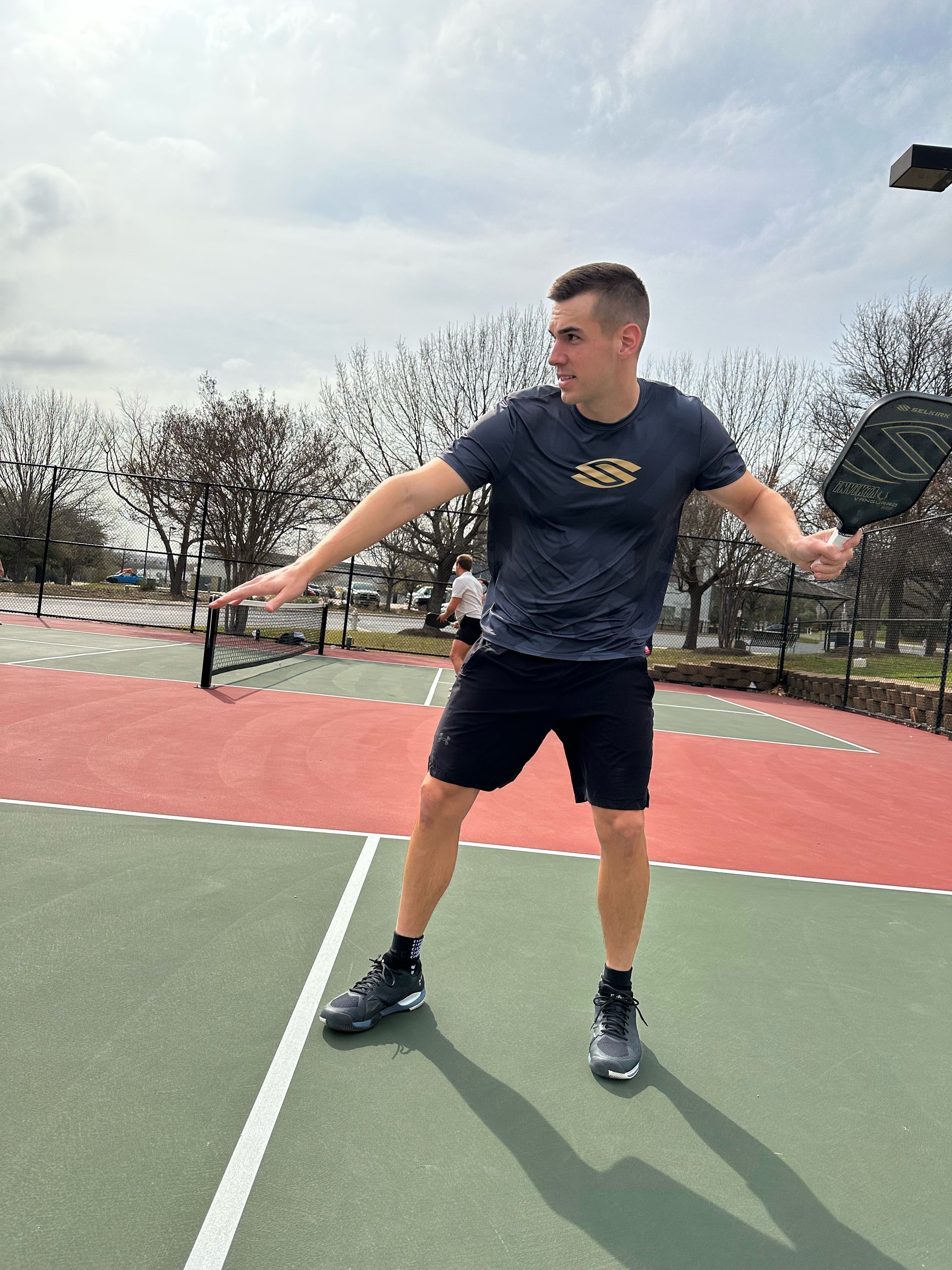 A male pickleball player in a black shirt preparing to hit a ball on a court.