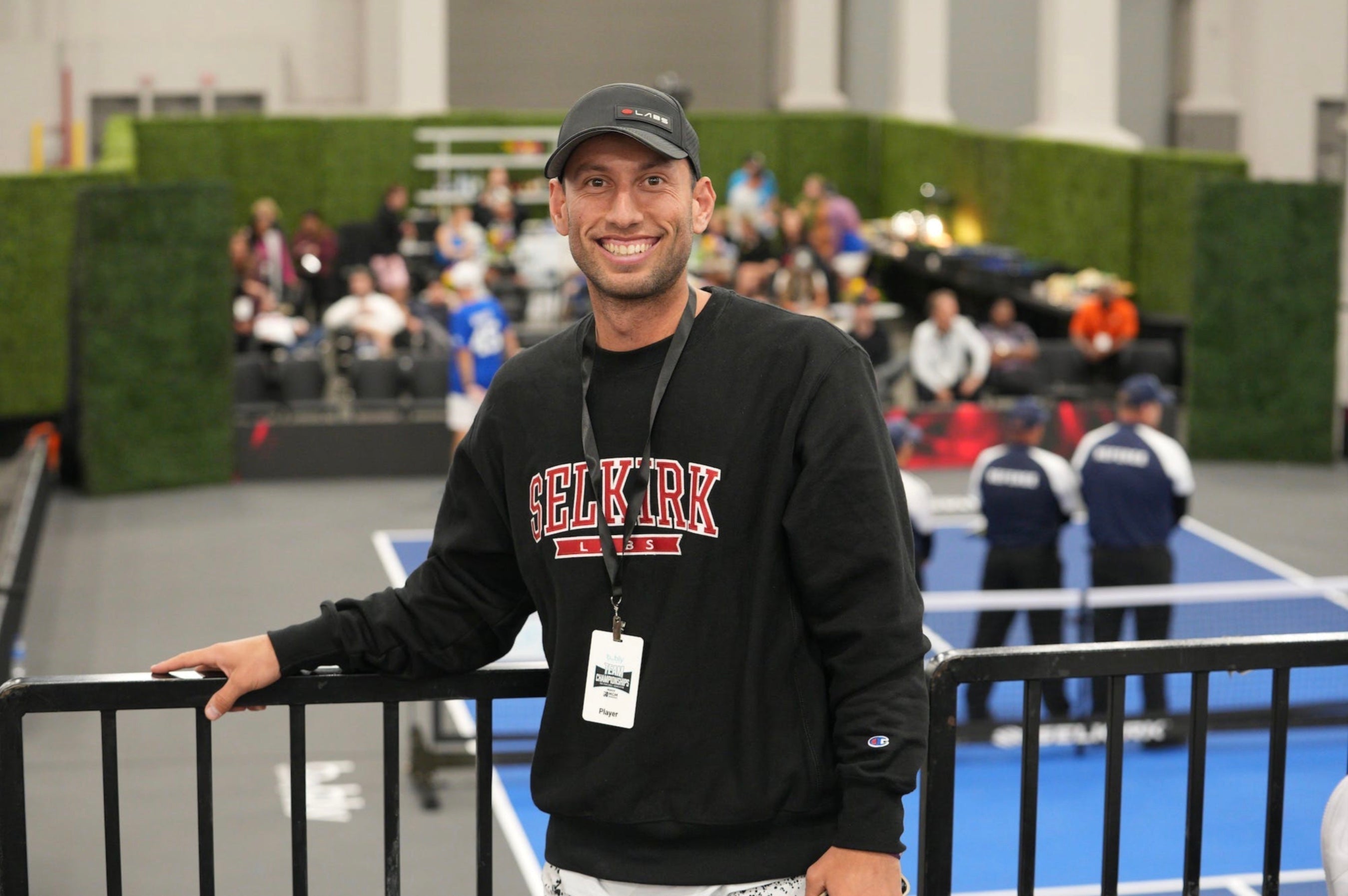 A smiling man wearing a Selkirk sweatshirt at a pickleball event.
