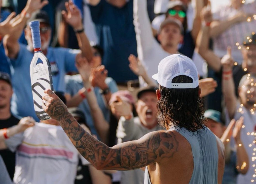A man with tattoos holding a trophy while celebrating with a crowd in the background.
