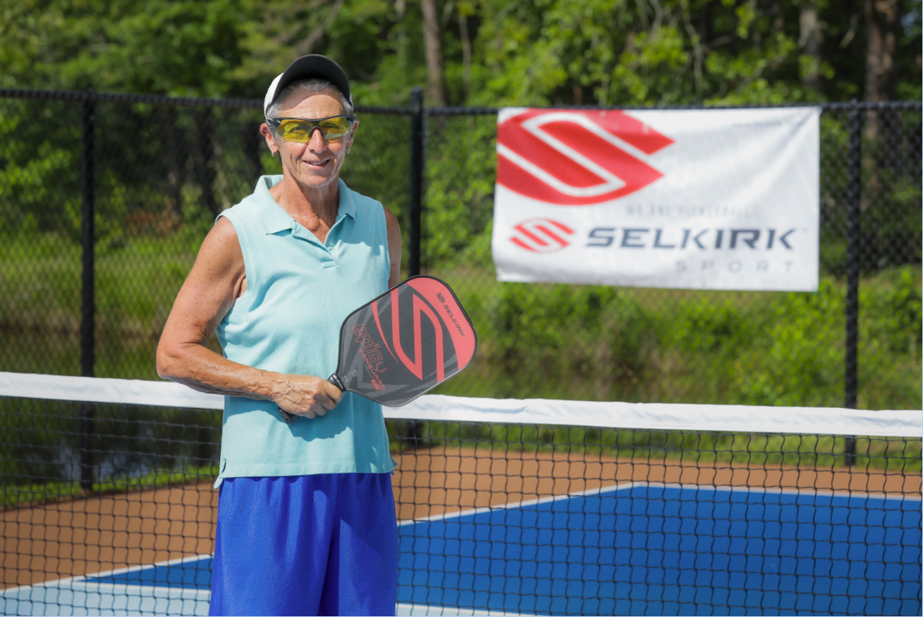 Eva Martin holding a Selkirk paddle on a pickleball court with a Selkirk banner in the background