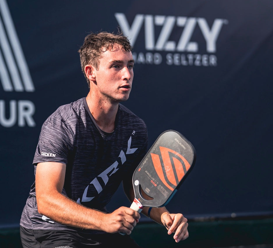 A male pickleball player preparing to serve, wearing a black shirt and holding a paddle.