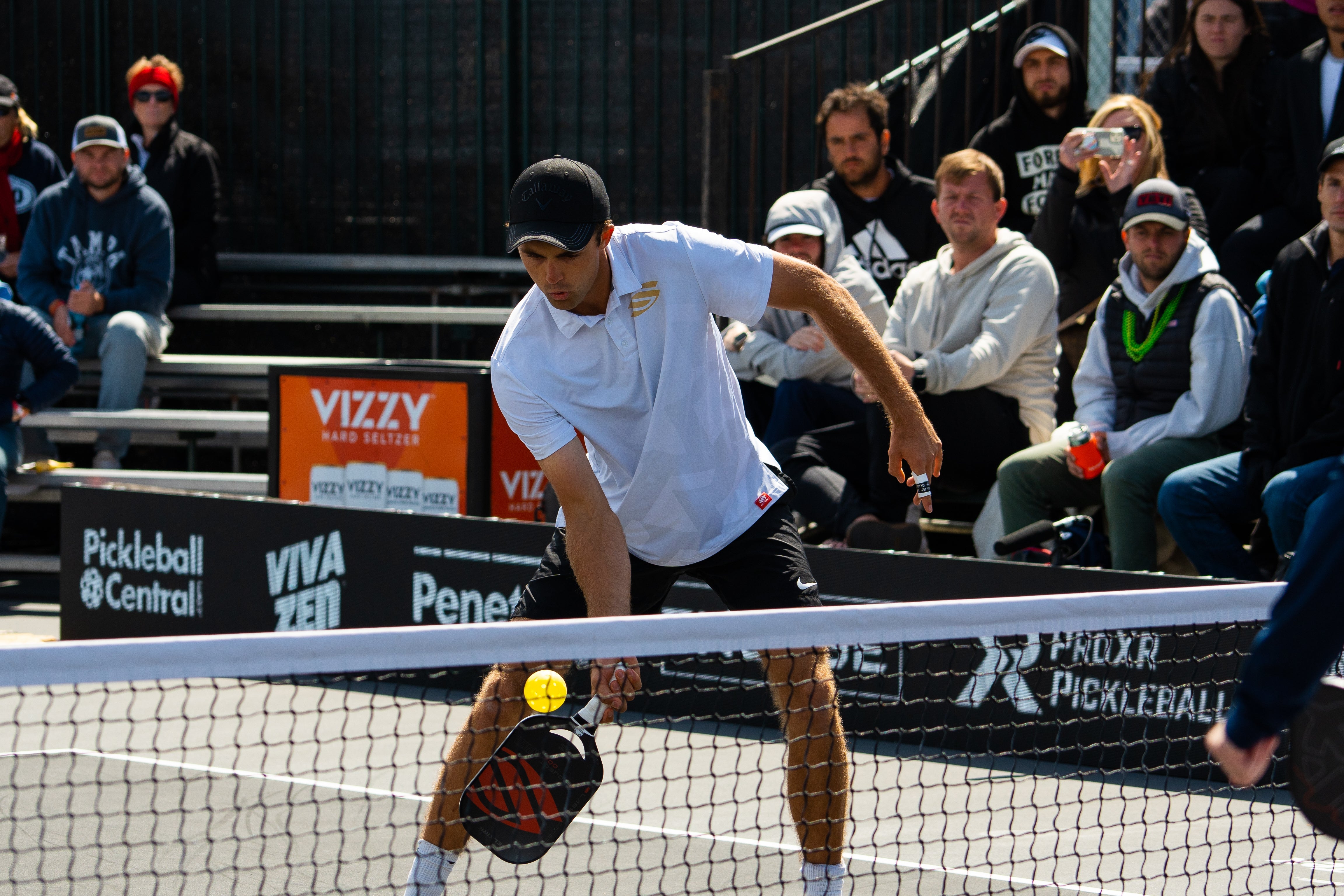 A player executing a shot during a pickleball match with spectators in the background.