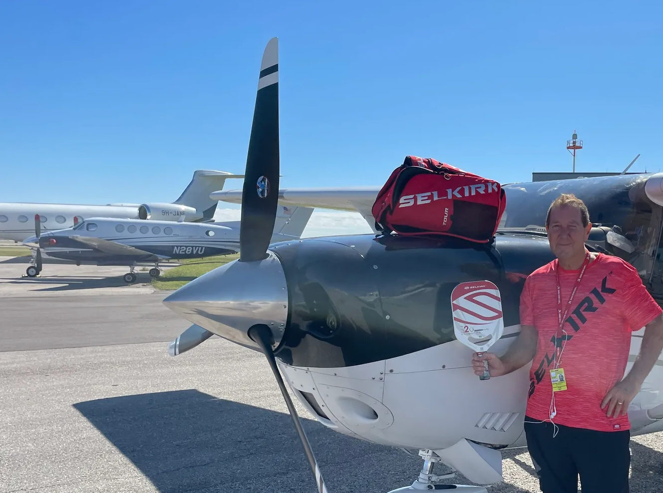 Dean Matt, The Pickleball Pilot, stands next to his aircraft with a Selkirk Sport bag and paddle.