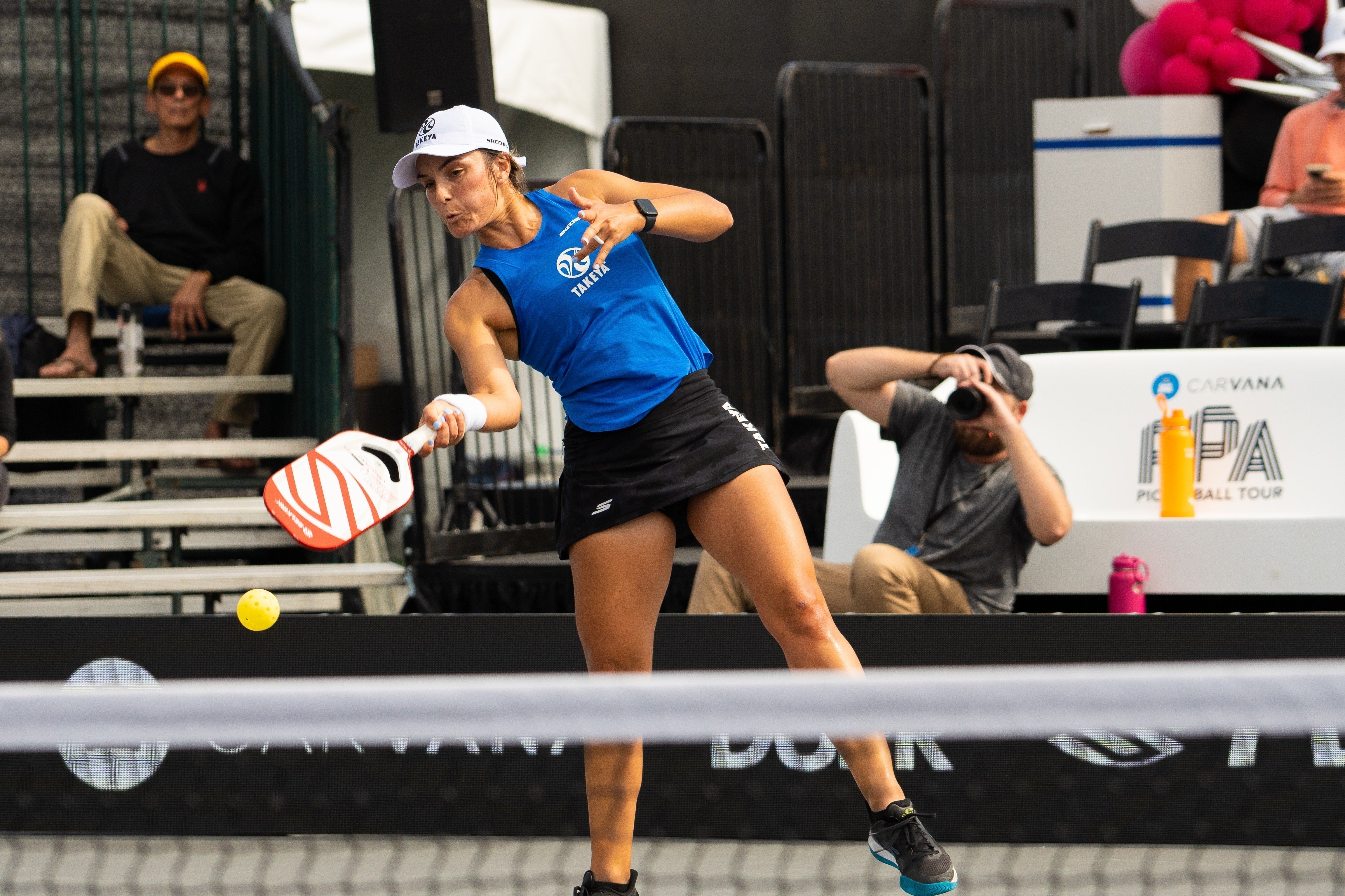 A female pickleball player in a blue shirt hitting a ball during a match.