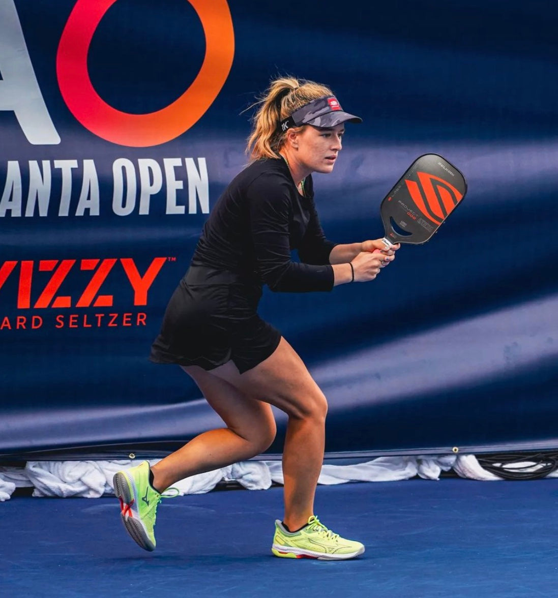 A female pickleball player in action, wearing a black outfit and preparing to hit the ball.