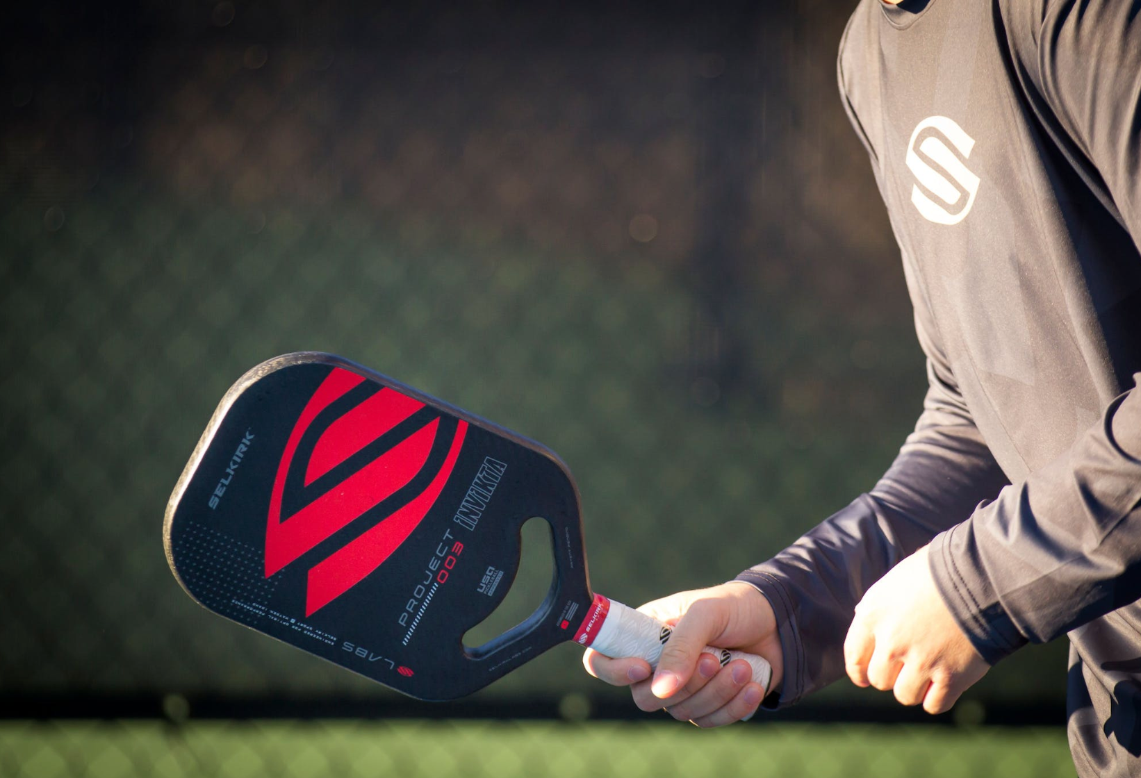 Close-up of a hand holding a pickleball paddle with a red design.