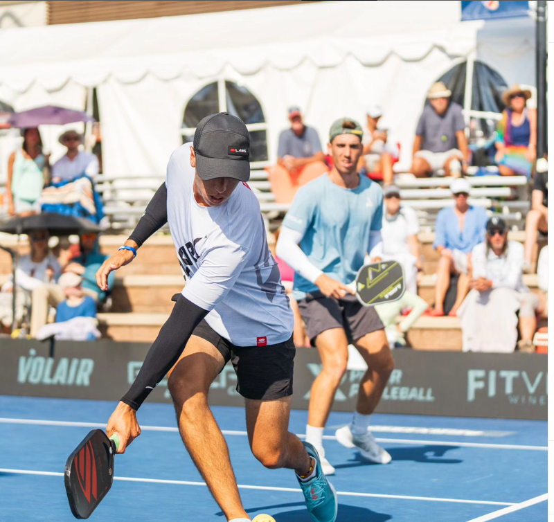 Two male pickleball players competing at the PPA Denver Open, one in a white shirt and black cap, the other in a light blue shirt.