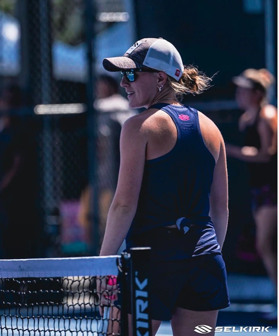 Female pickleball player in athletic wear at the Tournament of Champions, with a net in the foreground.